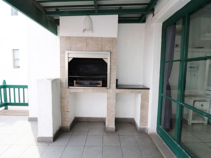 A covered balcony featuring a built-in braai, tiled flooring, and direct access to the interior through a large glass sliding door.