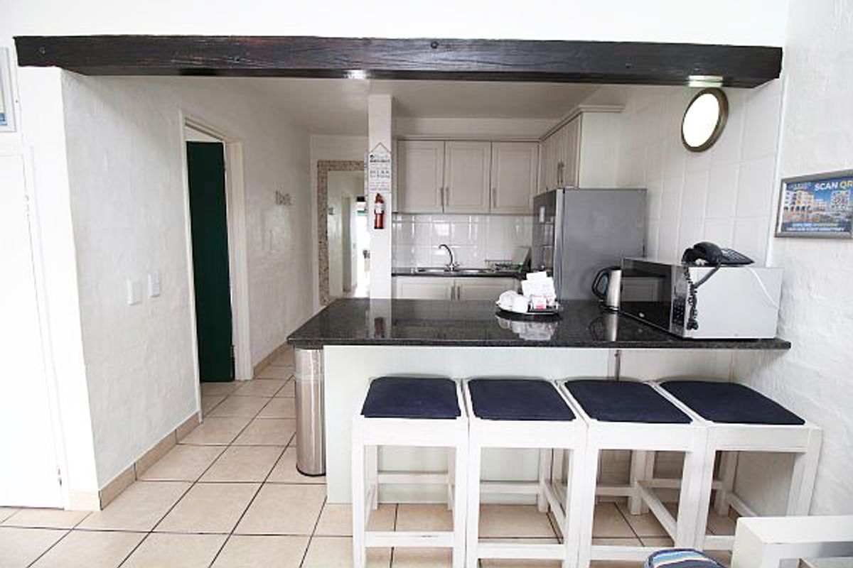 A functional kitchen area featuring granite countertops, built-in cabinetry, and tiled flooring, accented by a prominent exposed timber beam.