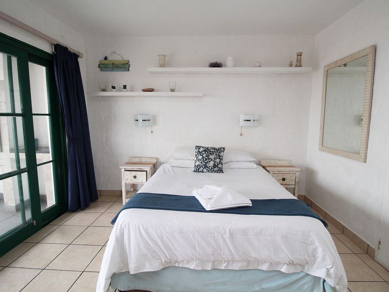 A bedroom featuring tiled flooring, built-in floating shelves, wall-mounted lighting, and a sliding glass door providing access to an outdoor area.