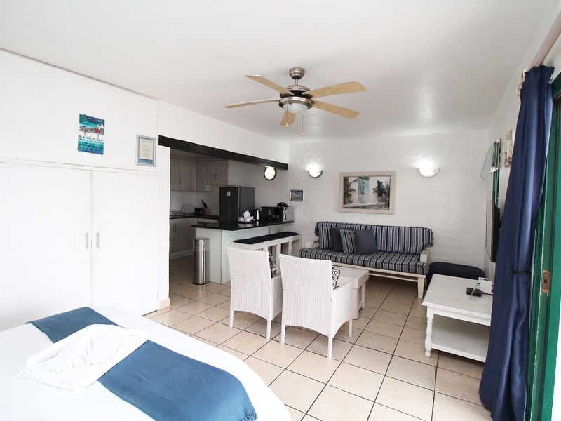 Open-plan living area featuring tiled floors, a ceiling fan, and a compact kitchen with built-in cabinetry, seamlessly connected to the living space.
