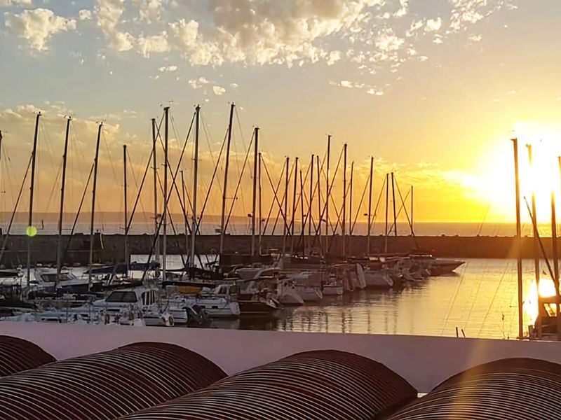 A scenic sunset view overlooking a marina filled with sailboats and yachts, captured from an elevated vantage point.