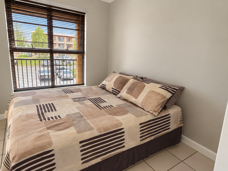 A well-maintained bedroom featuring neutral wall tones, tiled flooring, and venetian blinds providing natural light.