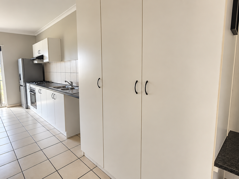 A clean, functional kitchen featuring white cabinetry, built-in oven, gas cooktop, tiled splashback, and direct access to a balcony.