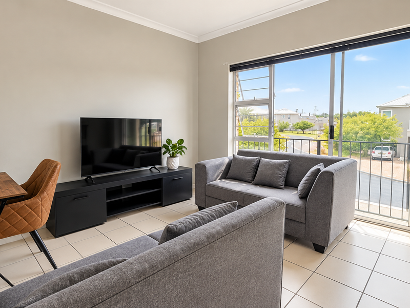 A bright living room featuring tiled flooring and a large sliding glass door leading to a balcony with neighborhood views.