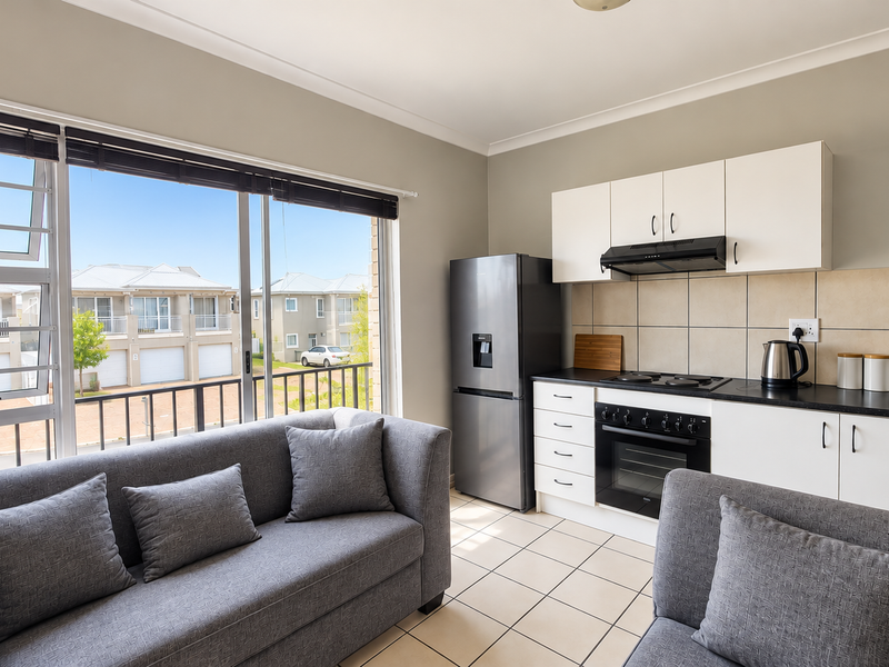 Bright open-plan living area featuring a modern kitchen with built-in appliances, tiled flooring, and large sliding doors leading to a balcony.