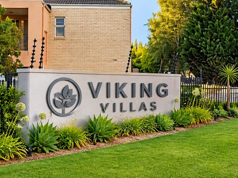The entrance to Viking Villas featuring well-maintained landscaping, secure metal perimeter fencing, and clear complex signage.