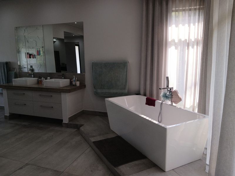 Modern bathroom featuring a freestanding bathtub on a raised platform, double vanity with vessel sinks, and large wall mirror with neutral finishes.