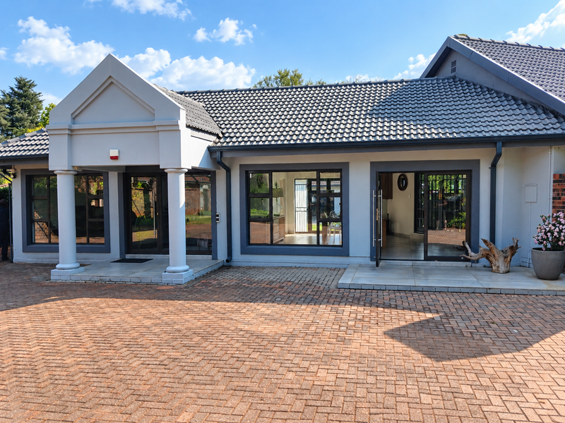 Front elevation of a modern house featuring a paved driveway, tiled roof, concrete columns, and large aluminium-framed windows and sliding doors.