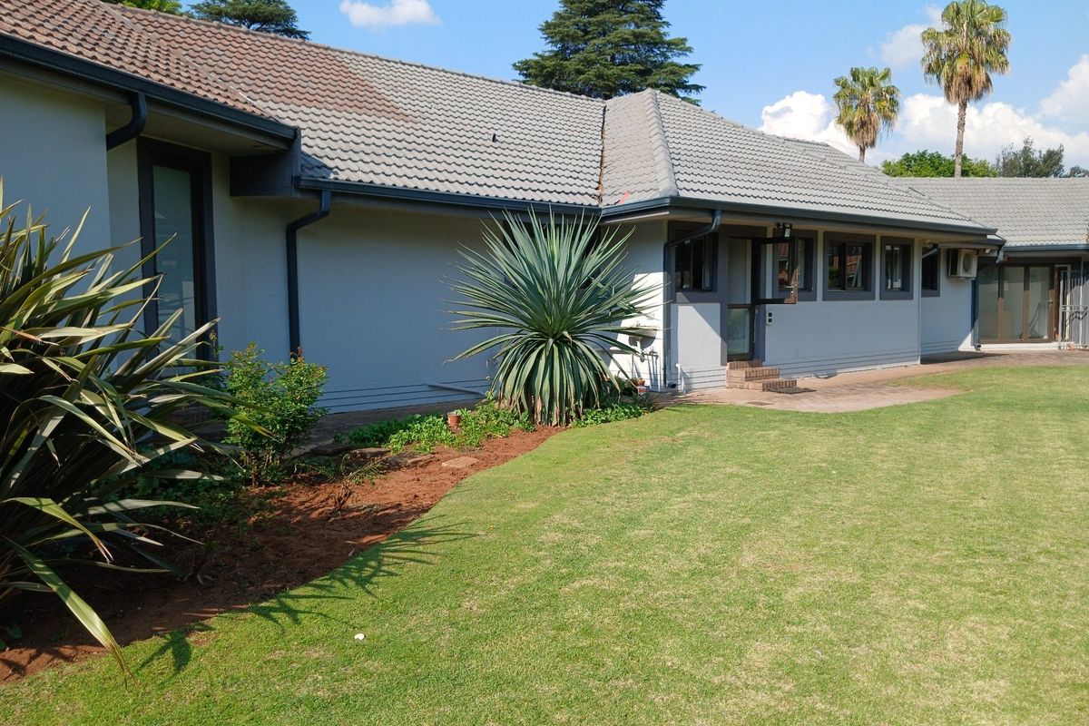 A well-maintained rear exterior view of the house featuring a tiled roof, paved walkway, and a neat, landscaped lawn.