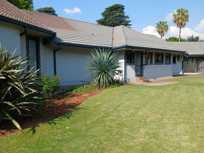 A well-maintained rear exterior view of the house featuring a tiled roof, paved walkway, and a neat, landscaped lawn.
