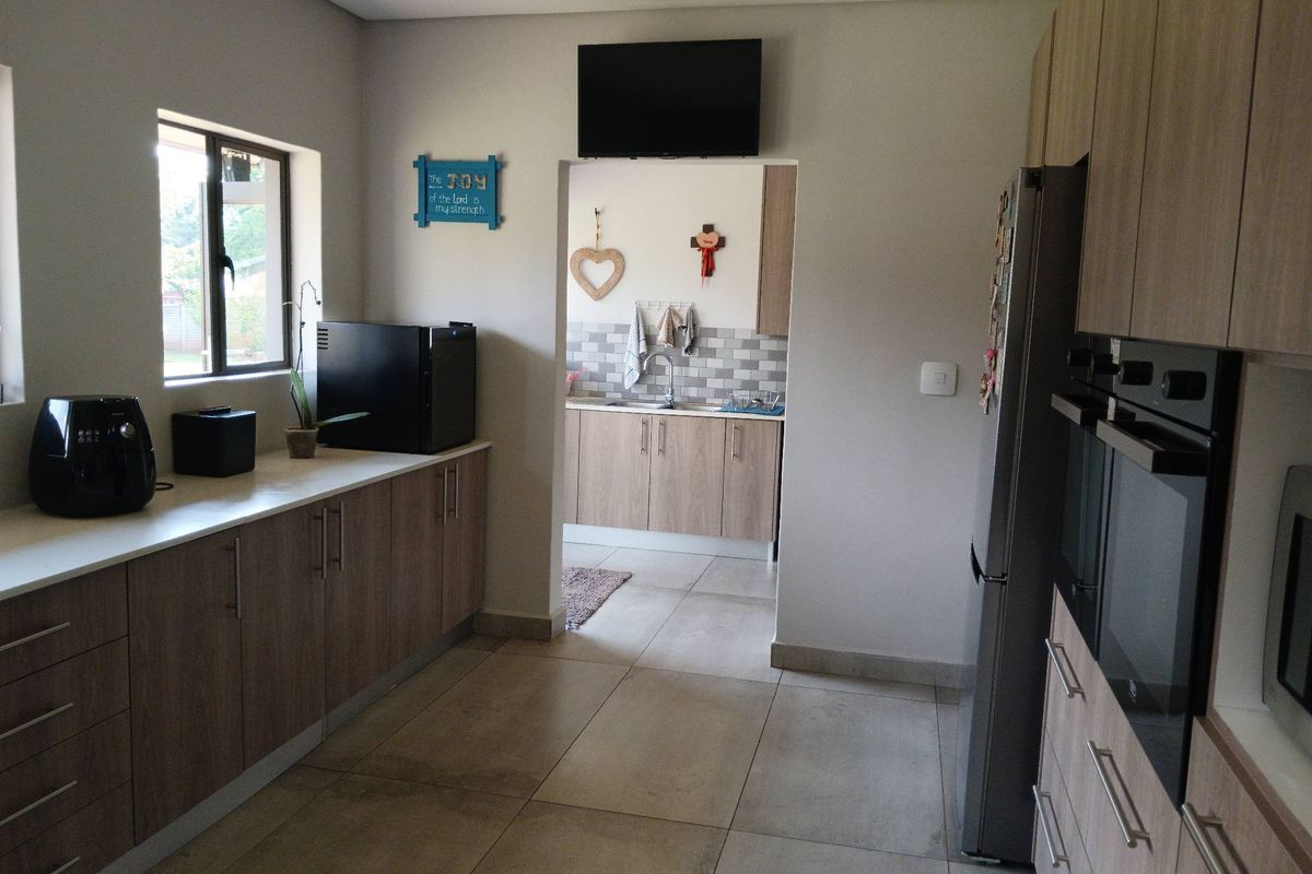 Modern kitchen featuring light wood-tone cabinetry, stone countertops, tiled flooring, and integrated double wall ovens, with an adjacent scullery area.