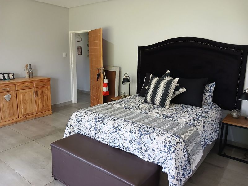 A well-maintained bedroom featuring neutral wall tones, large format floor tiles, and a solid wood door leading to an adjacent space.