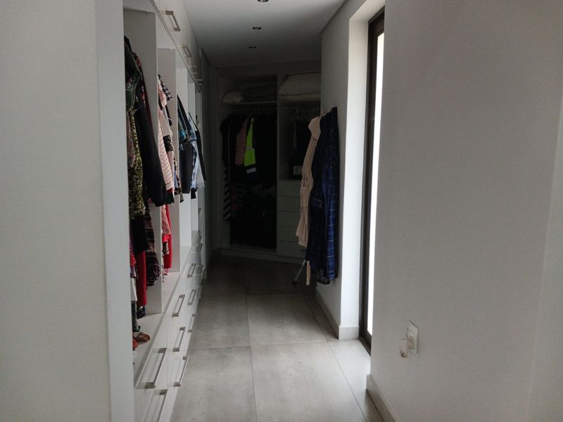 A walk-in closet featuring extensive built-in cabinetry, recessed ceiling lighting, and large format floor tiles with direct access to an outdoor area.