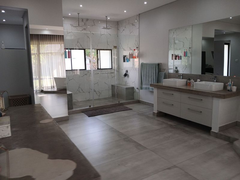 Spacious modern bathroom featuring a double vanity, large walk-in shower with marble-look tiling, and a separate freestanding bathtub in a bright, open layout.