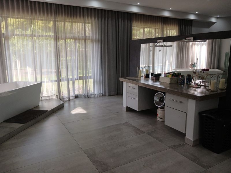 Spacious modern bathroom featuring a freestanding bathtub, double vanity with stone countertop, and large windows with floor-to-ceiling curtains.