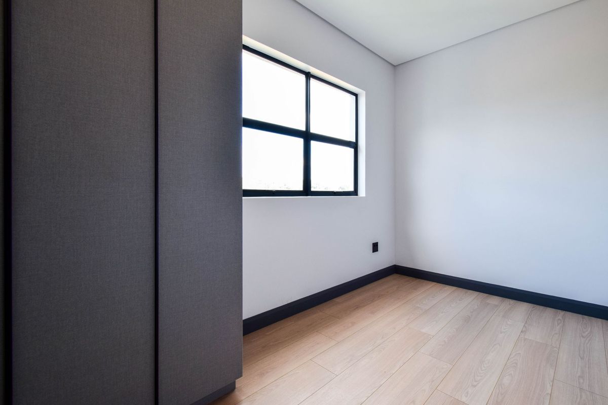 A bright, modern bedroom featuring light wood-look flooring, dark skirting boards, and a built-in wardrobe with a textured finish.