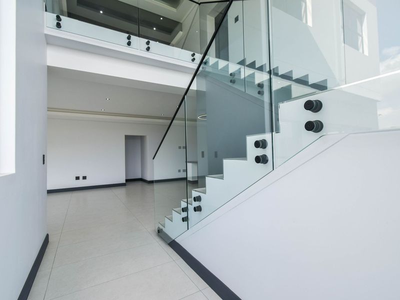 Modern open-plan living area featuring a striking staircase with frameless glass balustrades, sleek tiled flooring, and a mezzanine level overlooking the space.