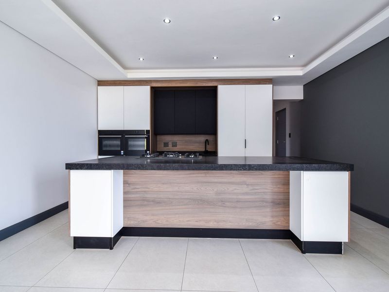 Modern kitchen featuring a large central island with a built-in gas hob, dual wall ovens, and contemporary two-tone cabinetry with stone countertops.