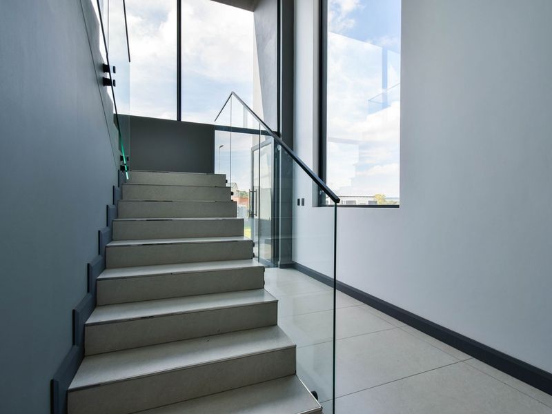 Modern staircase featuring tiled steps, a frameless glass balustrade, and expansive floor-to-ceiling windows that provide abundant natural light.