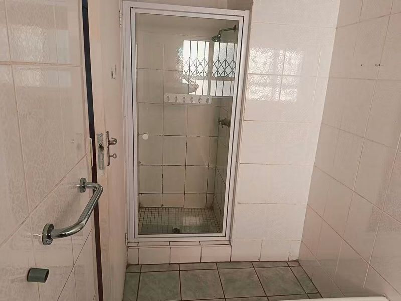A functional bathroom featuring a tiled shower enclosure with a security gate and a wall-mounted grab rail.
