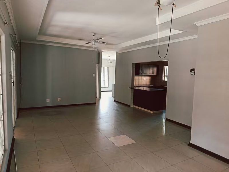 Spacious open-plan living area featuring tiled flooring, coved cornicing, and a connected kitchen with built-in cabinetry and a breakfast bar.