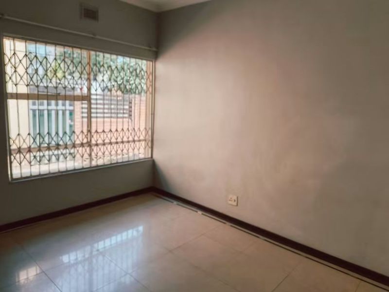 A vacant bedroom featuring tiled flooring, neutral walls, and a large window fitted with a security gate.
