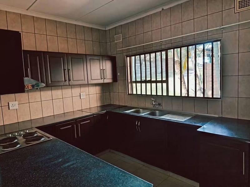 A functional kitchen featuring dark built-in cabinetry, laminate countertops, a double basin sink, and a built-in hob with tiled wall finishes.