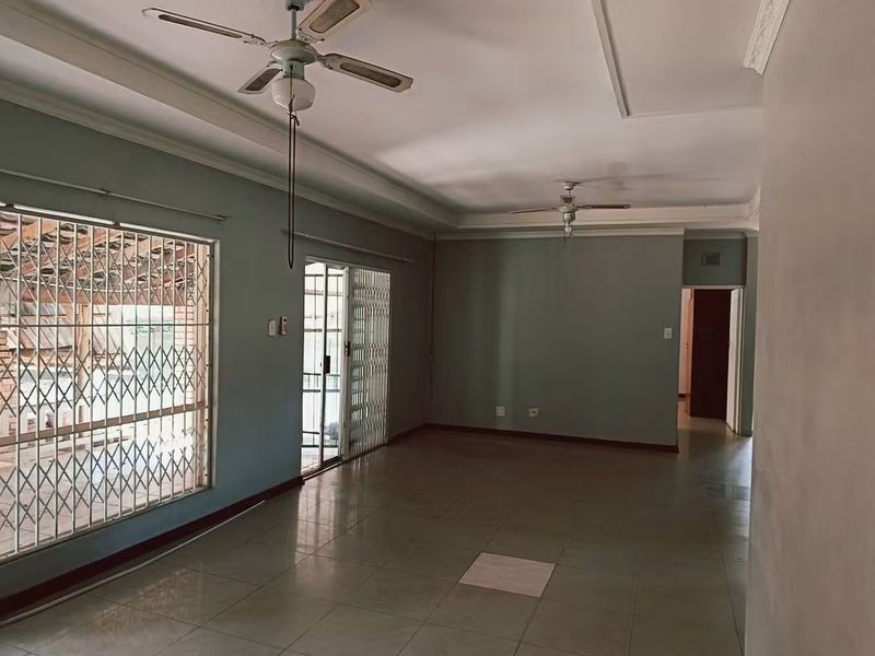 Spacious, empty living area featuring tiled flooring, ceiling fans, and sliding glass doors with security gates leading to the exterior.