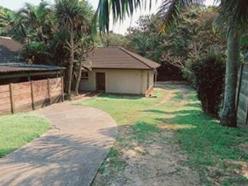 Rear view of the property featuring a tiled roof dwelling, concrete driveway, and established garden area enclosed by boundary walls.