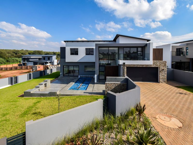 Modern double-story residence featuring a paved driveway, double garage, swimming pool with cover, and landscaped garden area.