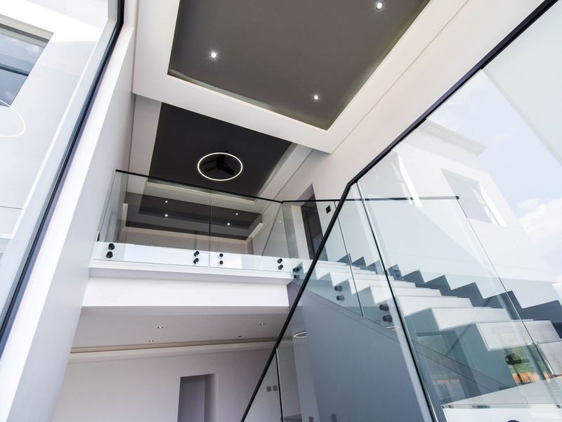 Modern double-volume entrance hall featuring a glass balustrade staircase and contemporary recessed ceiling lighting.