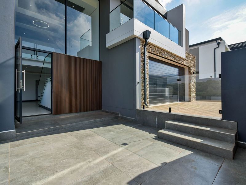 Modern architectural exterior featuring large glass windows, timber slat cladding, stone feature wall, and a paved entrance area with glass balustrades.