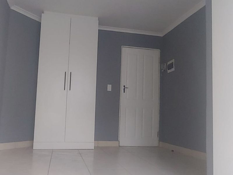 A clean, empty bedroom featuring neutral grey walls, white built-in wardrobe, tiled flooring, and a standard internal door.