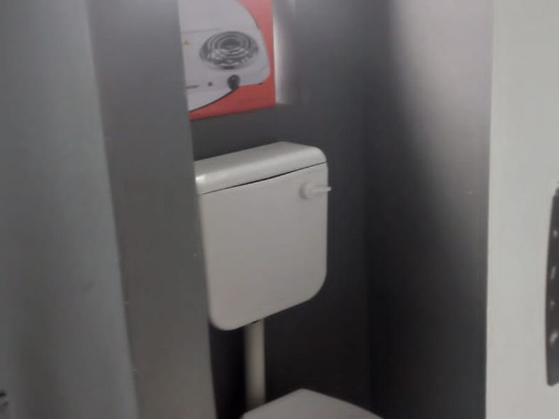 A compact, functional bathroom featuring a standard toilet, tiled flooring, and a small window for natural light.