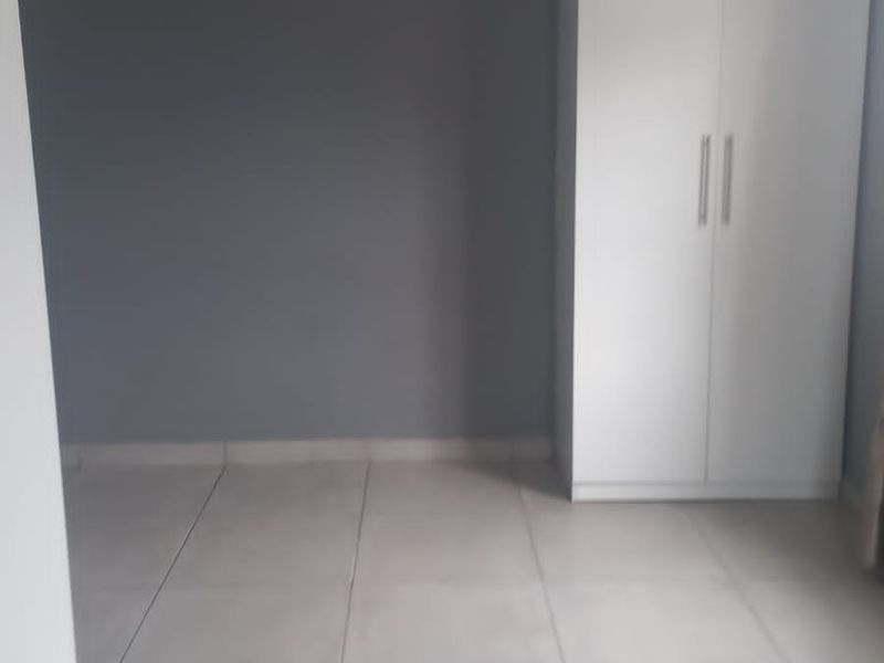 A clean, empty bedroom featuring neutral grey walls, large format floor tiles, and a white built-in wardrobe.