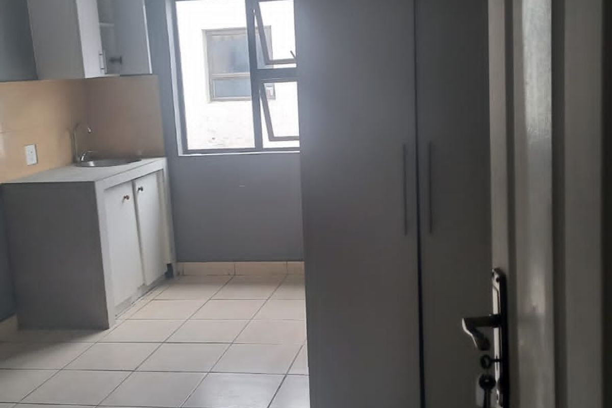 A compact kitchen area featuring tiled flooring, built-in cabinetry with a sink, and a large built-in storage cupboard.