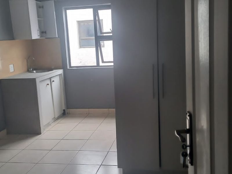 A compact kitchen area featuring tiled flooring, built-in cabinetry with a sink, and a large built-in storage cupboard.