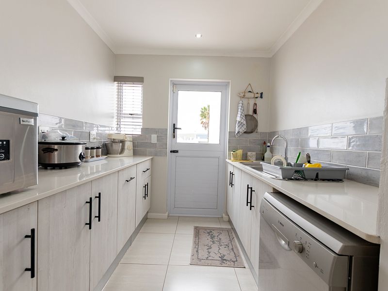 A clean and functional scullery featuring modern light-toned cabinetry, stone countertops, subway tile backsplash, and direct access to the exterior.