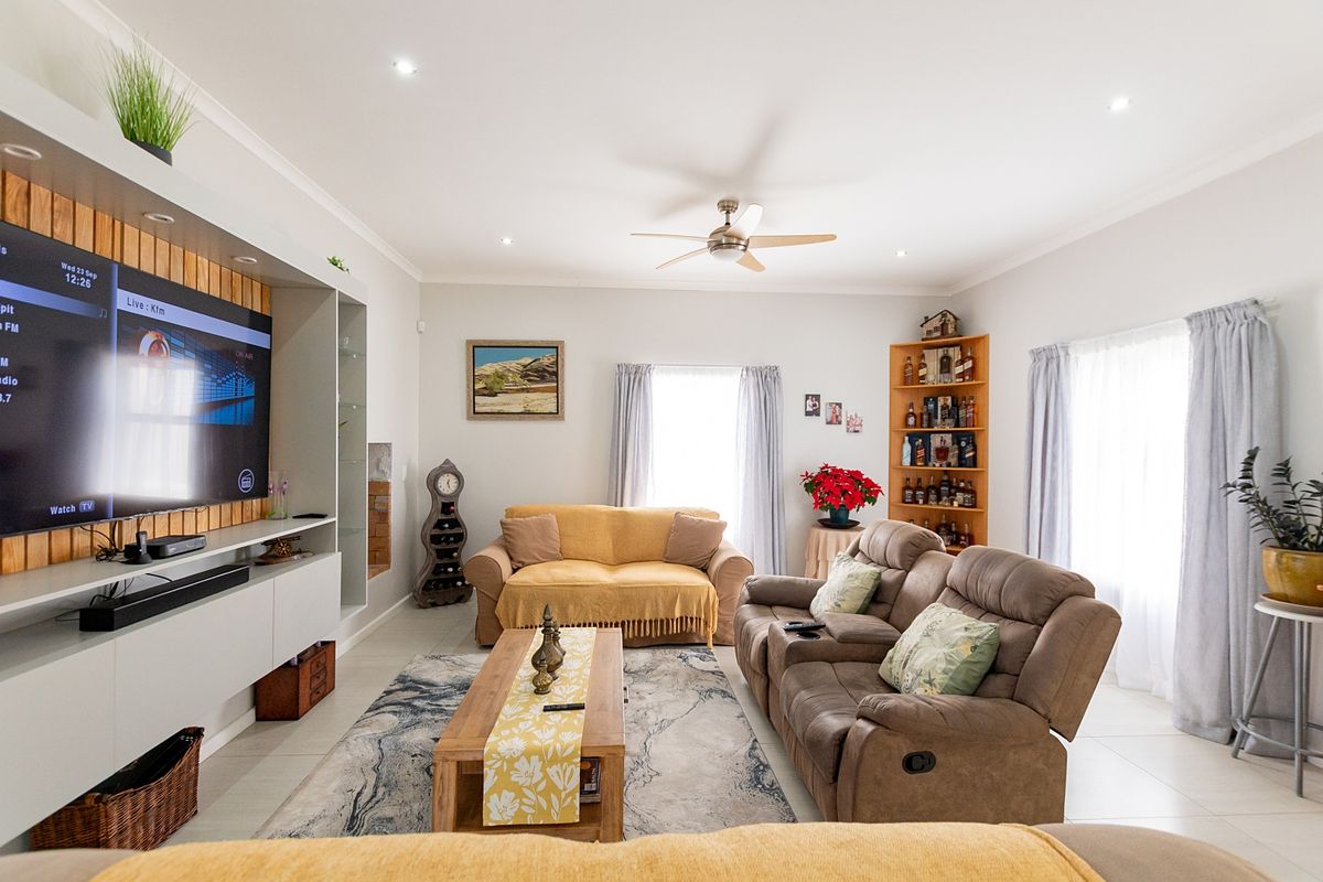 A well-maintained living room featuring a large built-in media unit, recessed ceiling lighting, a ceiling fan, and neutral tiled flooring.