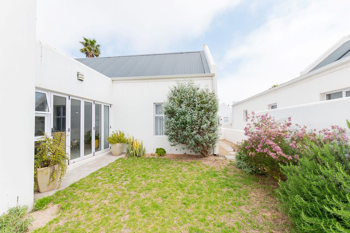 A private rear courtyard featuring a small lawn, paved pathway, and bi-fold glass doors providing seamless access to the interior living space.