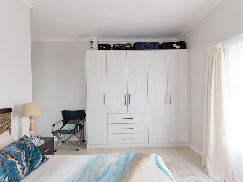 A well-maintained bedroom featuring a large, light-toned built-in wardrobe with integrated drawers and modern hardware.