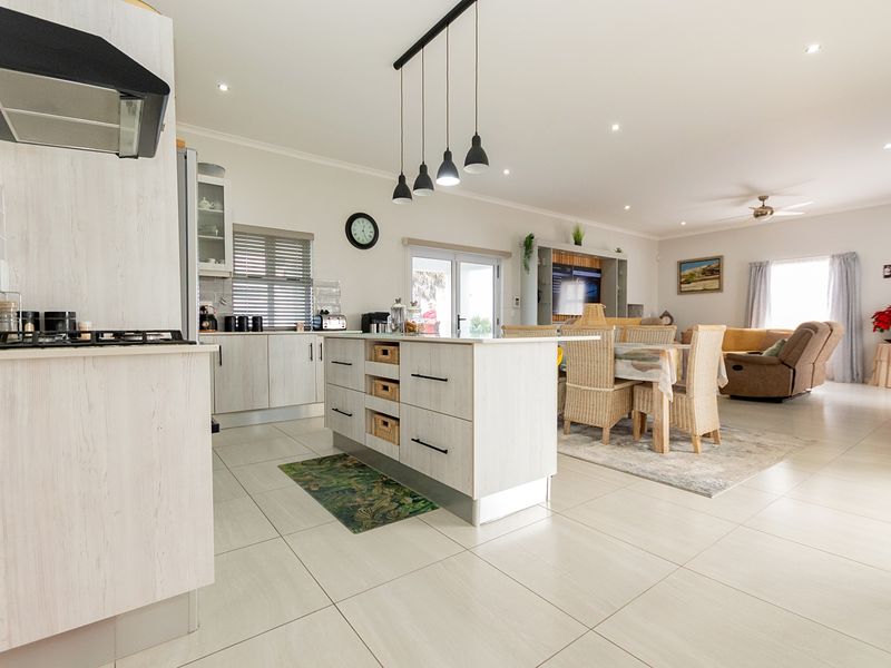 Spacious open-plan living area featuring a modern kitchen with a central island, gas hob, and light wood-finish cabinetry, flowing into the dining and lounge space.