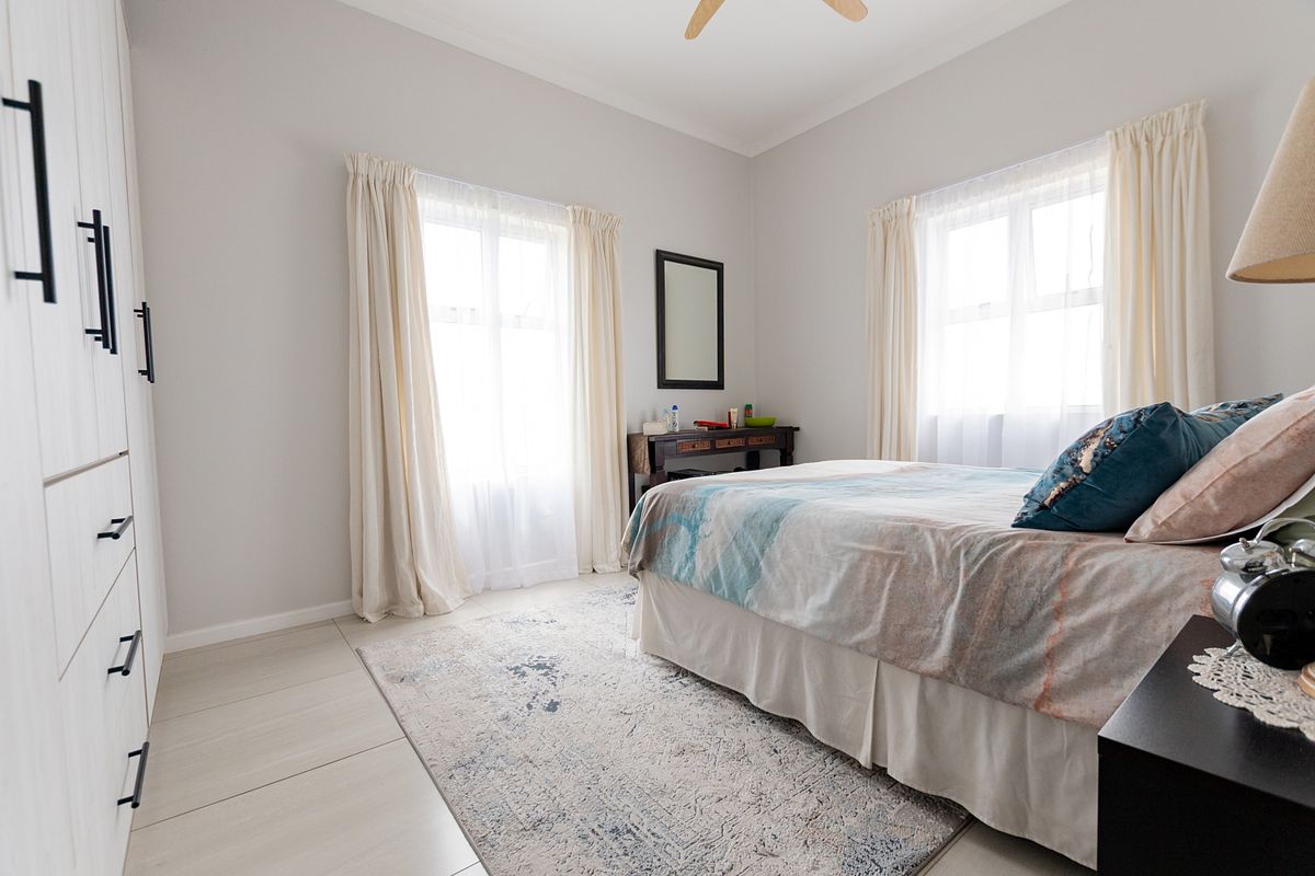 A bright and well-maintained bedroom featuring neutral tiled flooring, a spacious built-in wardrobe, and a ceiling fan.