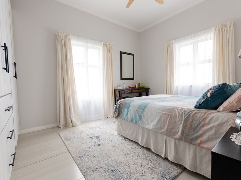 A bright and well-maintained bedroom featuring neutral tiled flooring, a spacious built-in wardrobe, and a ceiling fan.