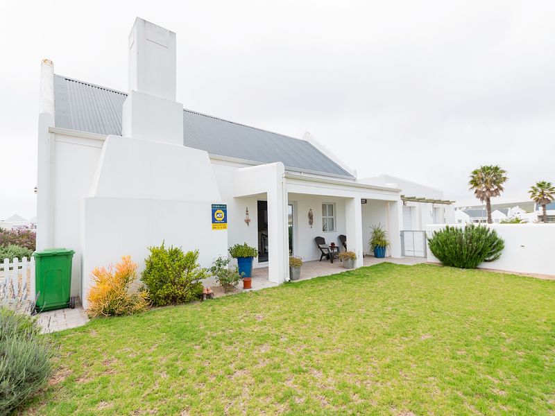 Rear view of the property featuring a white facade, corrugated metal roof, prominent chimney, and a covered patio overlooking a well-maintained garden.