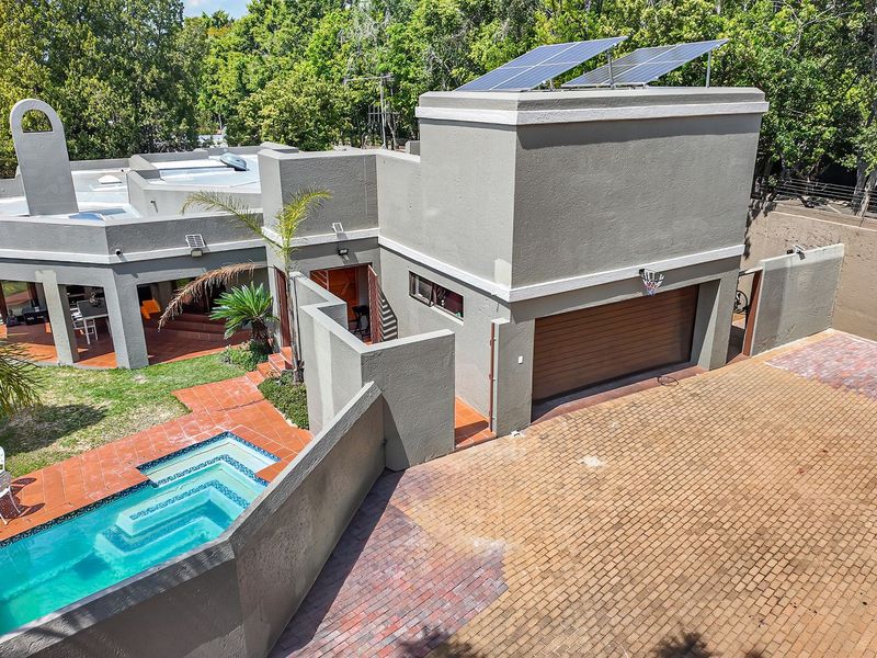 Aerial view of the property featuring a paved driveway, garage, swimming pool, and solar panels installed on the roof.