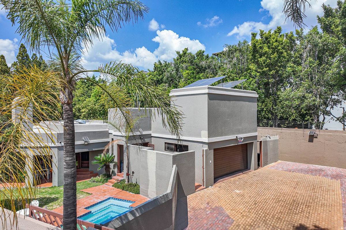 Rear exterior view of the property featuring a paved driveway, garage, swimming pool, and solar panels installed on the roof.
