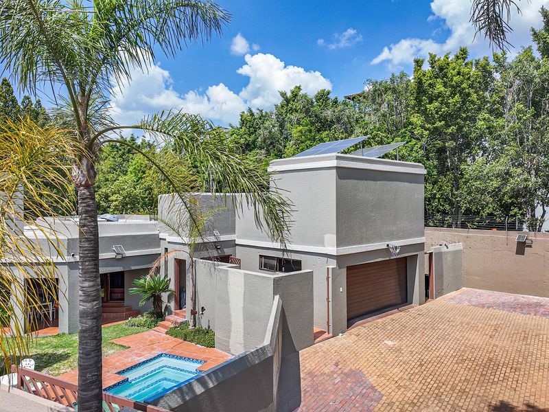 Rear exterior view of the property featuring a paved driveway, garage, swimming pool, and solar panels installed on the roof.