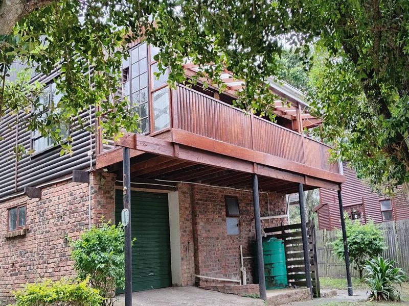 Rear view of a two-story house featuring an elevated timber balcony, exposed brick lower level, and a garage with a roller door.