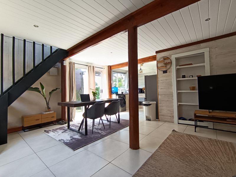 Open-plan living and dining area featuring tiled floors, exposed timber beams, a staircase, and direct access to the outdoor space through sliding glass doors.